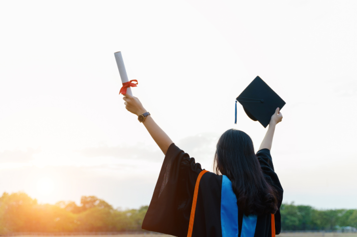A graduate holding their diploma an cap in the air